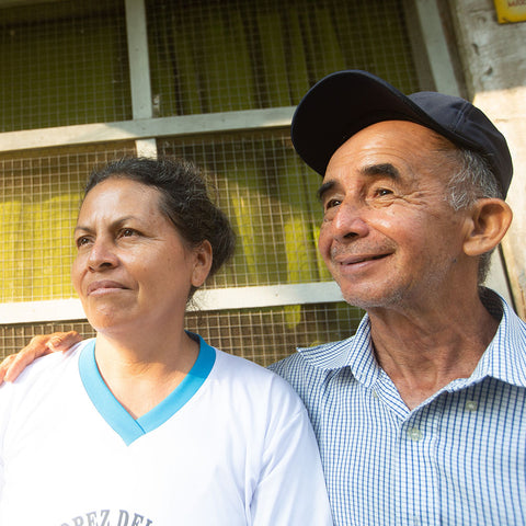 Nelita Paredes and Alberto Lopez Pena standing together in front of a screen panel window looking off to the left