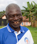 Komi Ebe Kenou, member of SCOOPS IKPA co-op in Togo smiling in front of banana trees and buildings