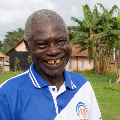 Komi Ebe Kenou, member of SCOOPS IKPA co-op in Togo smiling in front of banana trees and buildings