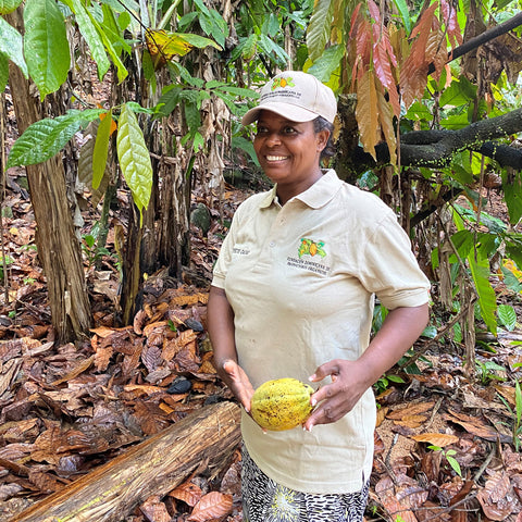 Elisa Done Frias of FUNDOPO co-op holds a yellow cacao pod in her hands in front of her cacao farm in the Dominican Republic