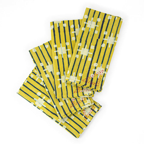 Four folded fabric napkins arranged in a fan shape. The napkins feature a pattern of yellow, blue, and white stripes with abstract geometric designs. The background is plain white.