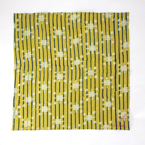 A yellow square fabric with a pattern of vertical black stripes and light-colored geometric shapes, resembling abstract pluses and dots, arranged in a grid-like pattern.