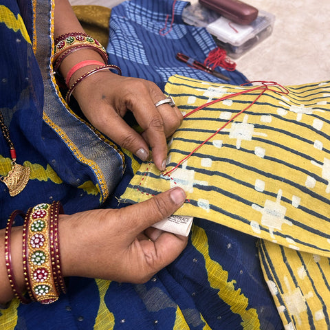 Two hands embroidering a yellow napkin with red thread.