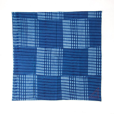 A blue square fabric with a grid pattern formed by small, light blue rectangles and lines. There is a small, red triangular stitching detail in one corner.