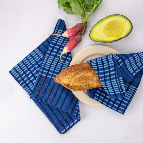 Blue striped napkins arranged with a cut avocado, fresh radishes, and a piece of crusty bread on a small plate.