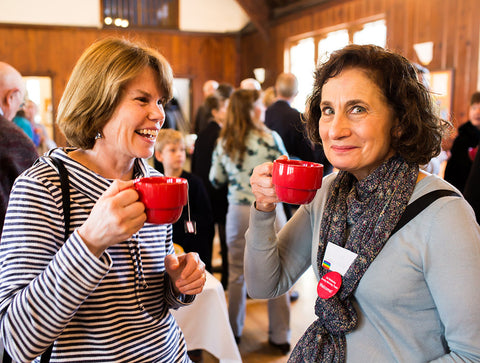 two women at a community gathering holding red mugs of brewed Equal Exchange tea