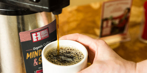 hand holding mug while pouring Equal Exchange coffee from airpot