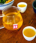 Glass pitcher of golden turmeric ginger tea next to two filled cups on a wooden tabletop