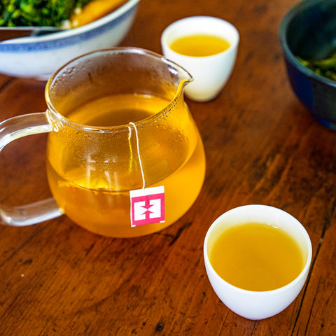 Glass pitcher of golden turmeric ginger tea next to two filled cups on a wooden tabletop
