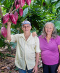 Juan Penalo and Nieve Quezada stand together in front of their cacao farm with reddish purple cacao pods growing from a cacao tree