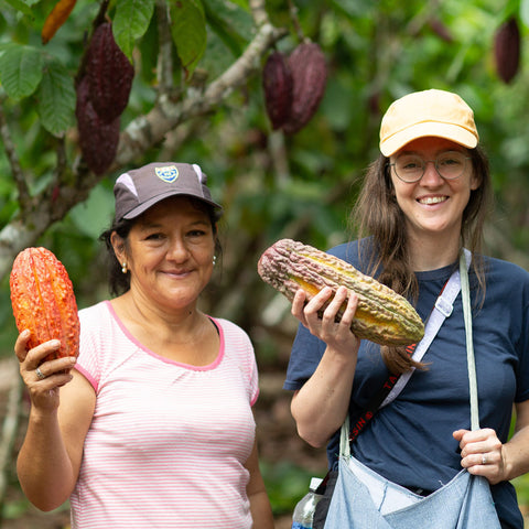 ACOPAGRO cacao farmer Candelaria Pena Villacorta stands with Equal Exchange's Katie Sharp while both are holding different colored cacao pods on a farm in Peru
