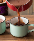 dark hot chocolate being poured from a pot into a mug ready to drink