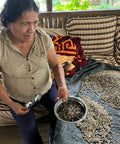 Woman holds a bowl of unroasted coffee beans with pile of more behind her