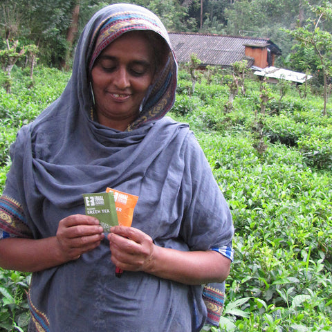 MOPA tea farmer holding Equal Exchange Green Tea and Ginger Tea envelope with her tea garden in the background 