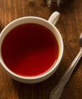 White mug filled with brewed tea on a wooden surface with a spoon and lavender flowers.
