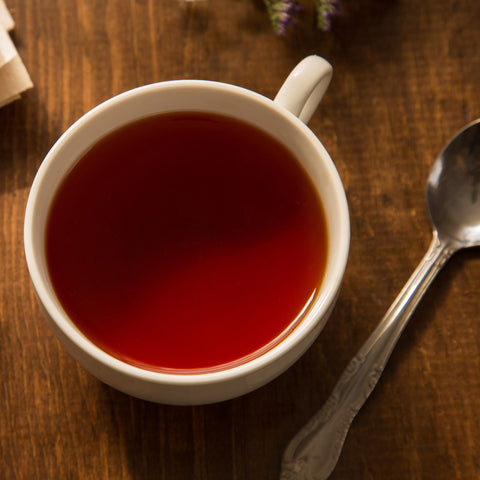 White mug filled with brewed tea on a wooden surface with a spoon and lavender flowers.