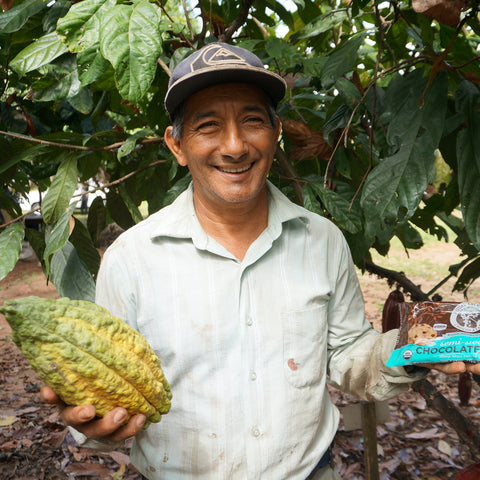 Miguel Rodriguez Rios holding a yellow and green cacao pod in one hand and a bag of Equal Exchange semi-sweet chocolate chips in the other hand
