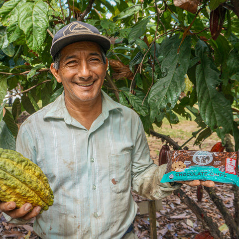 Cacao farmer and member of ACOPAGRO co-op holding a yellow cacao pod and a bag of Equal Exchange semi sweet chocolate chips on his farm in Peru