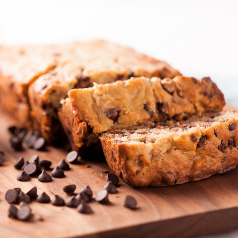 Loaf of chocolate chip banana bread sliced on a cutting board with chocolate chips scattered in front