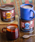 two cans of cocoa on a wooden table with two mugs of cocoa ready to drink