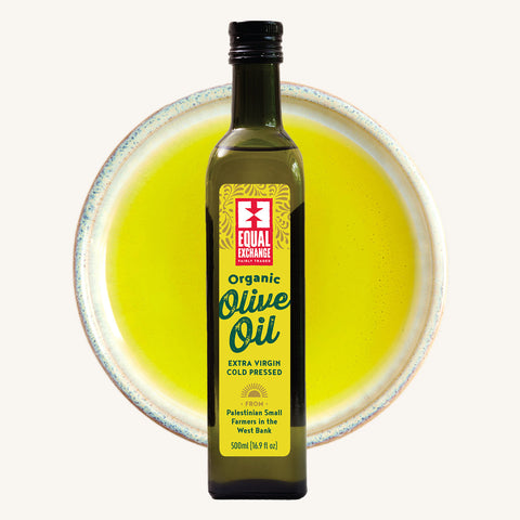 Bottle of Equal Exchange Olive Oil over a bowl of olive oil in background