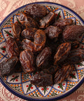 close up of dried medjool dates placed on a colorful plate with a lace tablecloth in the background