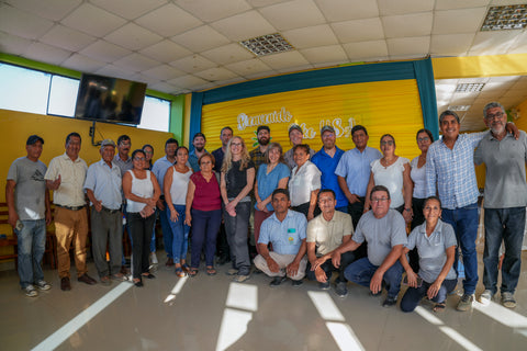A large group of people posing for a group photo inside a brightly lit room with yellow and green walls, a tiled ceiling, and a screen mounted on the wall.