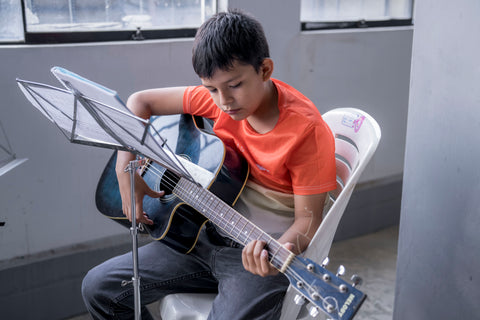 Boy sitting in classroom, with guitar and music stand