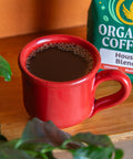 red mug filled with brewed coffee sitting on wooden table with green bag of coffee in background that says Organic Coffee House Blend