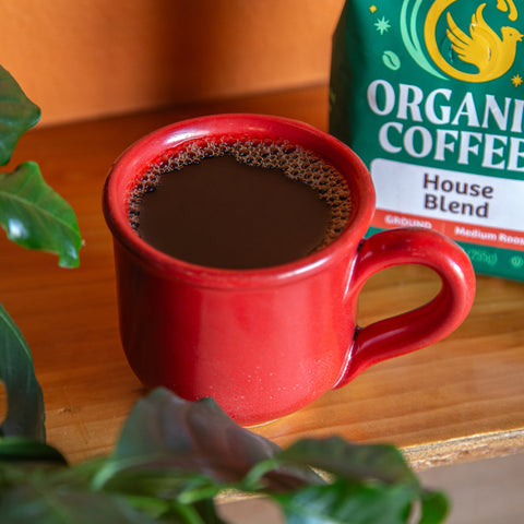 red mug filled with brewed coffee sitting on wooden table with green bag of coffee in background that says Organic Coffee House Blend