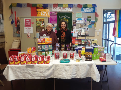 two people standing behind a table full of Equal Exchange products at a church table sale