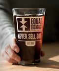 glass pint glass with white print on one side with Equal Exchange logo and text that reads Never Sell Out