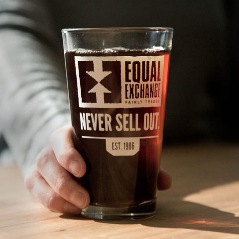 glass pint glass with white print on one side with Equal Exchange logo and text that reads Never Sell Out