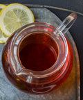 Clear tea pot filled with brewed Organic Earl Grey tea sitting on a metal tray with fresh lemon slices
