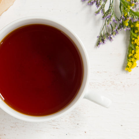 Cup of brewed Irish Breakfast tea on a white table with purple and yellow flowers