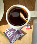 Cup of steeping Assam Black Tea with torn tea envelope on wooden table top