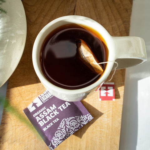 Cup of steeping Assam Black Tea with torn tea envelope on wooden table top