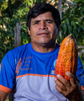 Javier Flores Garcia, member of ACOPAGRO co-op, holds up an orange and red cacao pod with cacao trees in the background