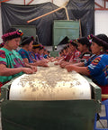 Women in Guatemalan traditional dress sorting coffee beans at a conveyor belt table
