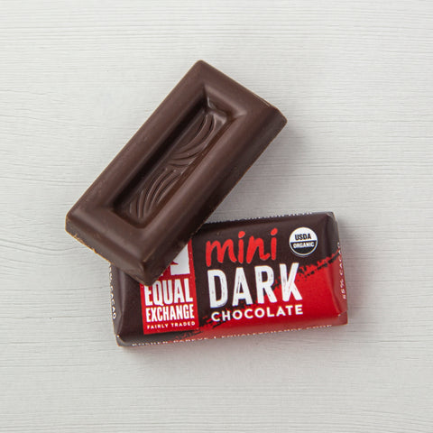 one unwrapped dark chocolate mini with one wrapped dark chocolate mini on a white wooden background
