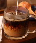 pouring cream into a glass mug of dark roast organic coffee