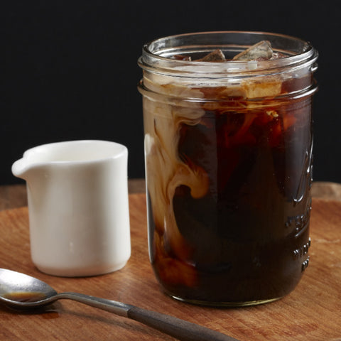 Mason jar filled with cold brew and ice cubes with cream poured in