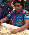 Woman in traditional Guatemalan dress sorting coffee beans on a conveyor belt