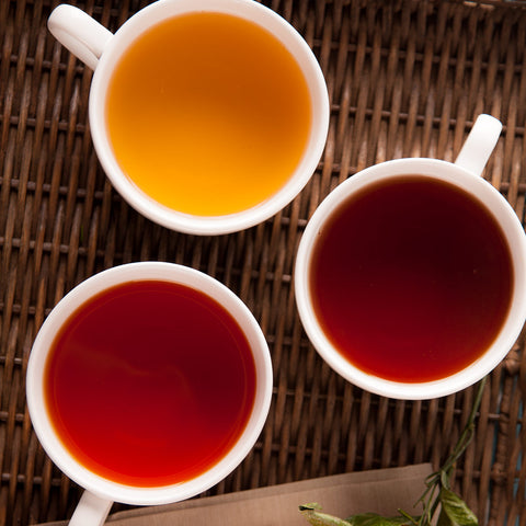 Three mugs of brewed tea ranging from red to yellow in color